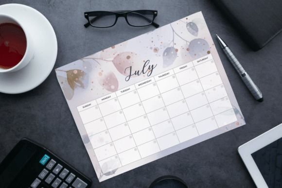 Printable monthly planner calendar for July with floral design on a desk with glasses, pen, calculator, and coffee cup